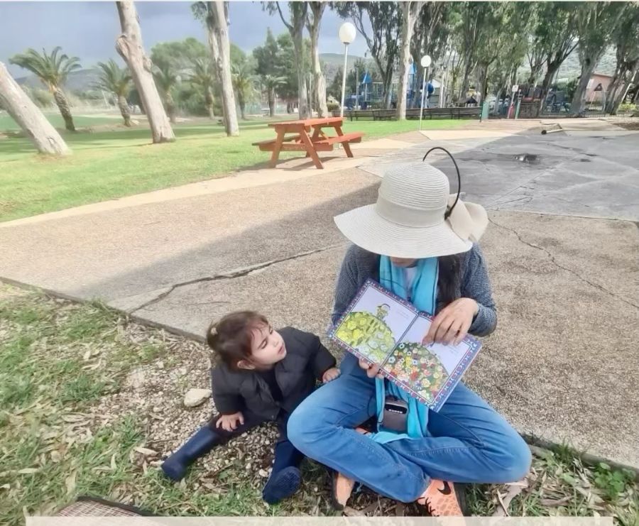 אשת צוות קוראת ספר לילדה בחצר