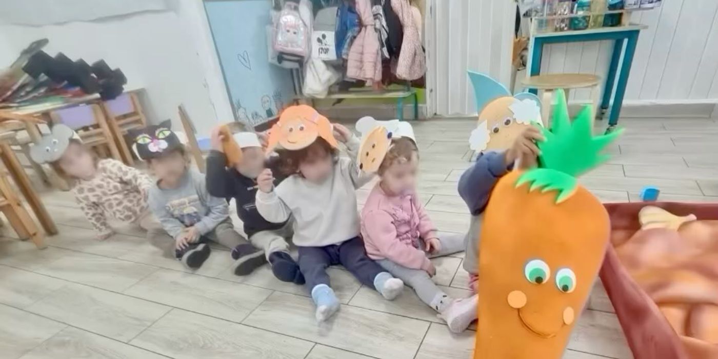 ילדים יושבים על הרצפה עם מסכות נייר, לצד אביזר גזר גדול