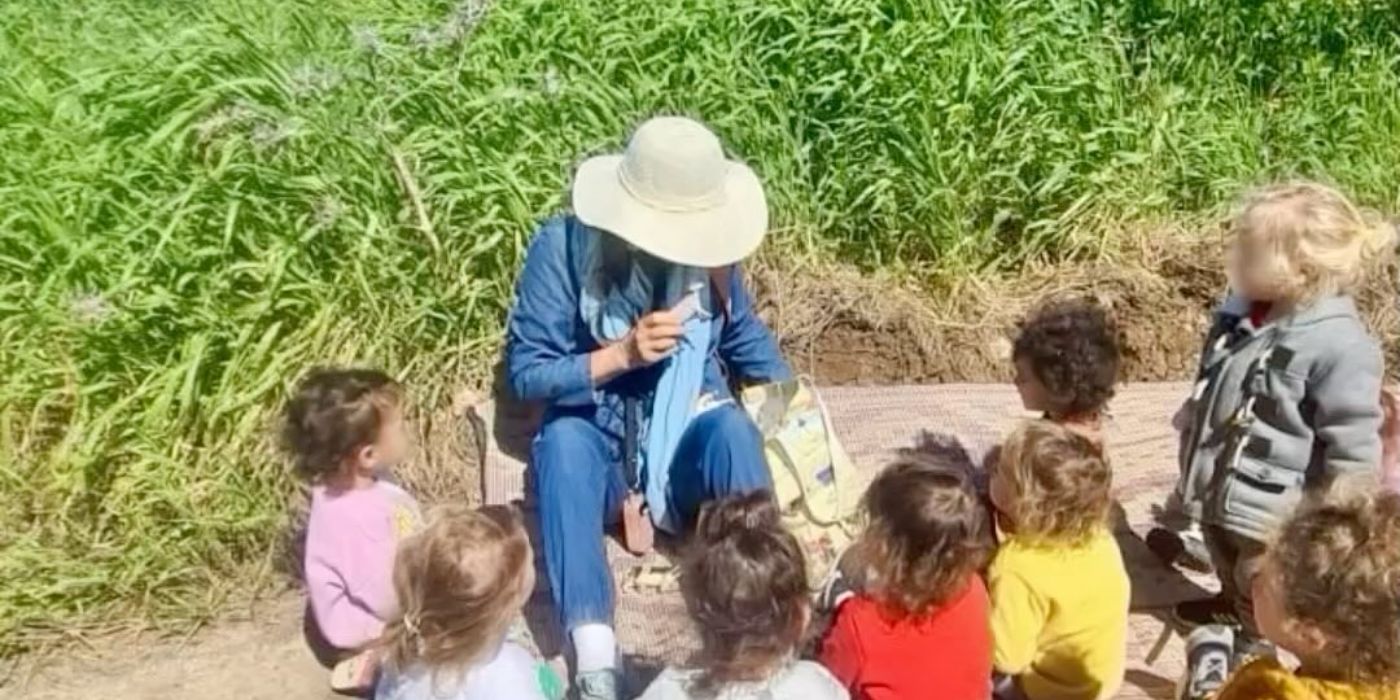אשת צוות יושבת עם קבוצת ילדים בשדה ירוק