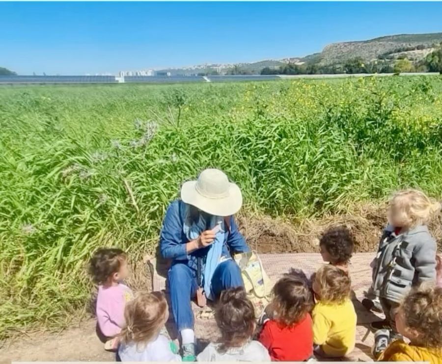 אשת צוות יושבת עם ילדים בשדה פורח
